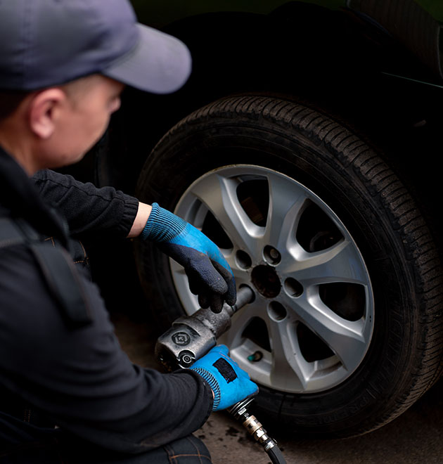 Auto mechanic in changing a wheel from black car