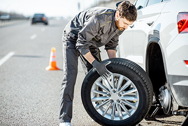 Worker changing car wheel on the highway