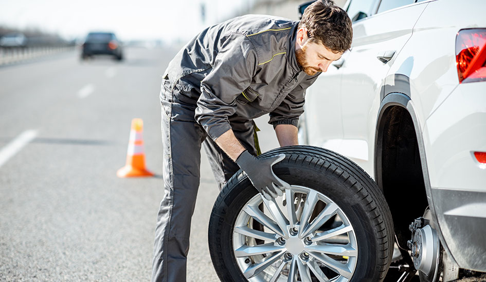 Worker changing car wheel on the highway